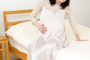 ベッドに手をつき片手でお腹を押さえ苦しんでいる妊婦