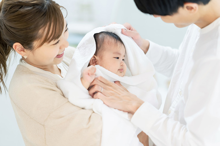 お母さんに抱かれながら頭を拭かれている赤ちゃん